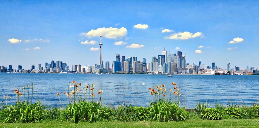 Image of Toronto skyline against a foreground of Lake Ontario and spring greenery.